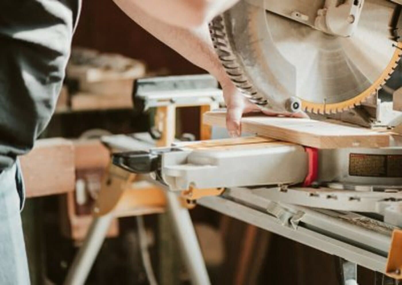 Hände an der Gehrungssäge in der Werkstatt, warmes Licht